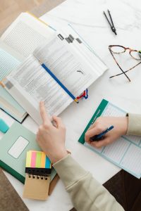 Close-up of a student studying with books and notes on a white desk.